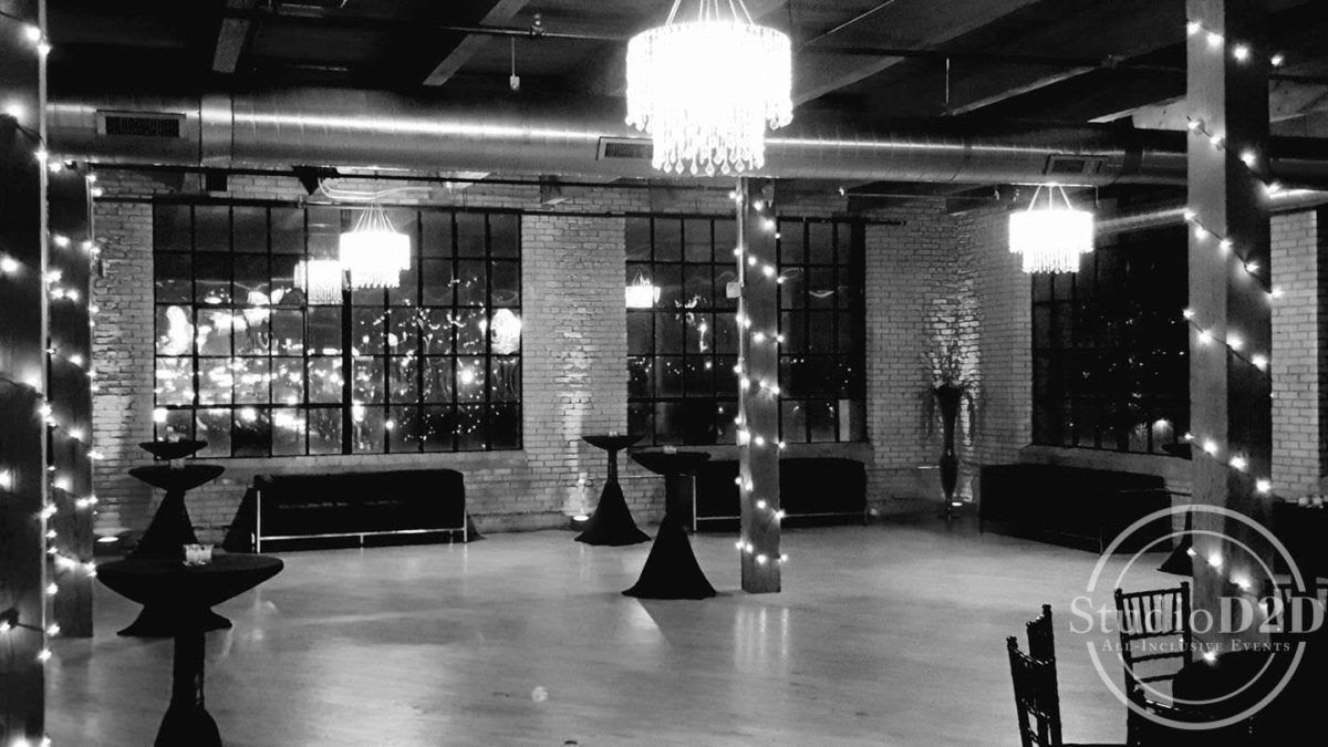 Empty banquet hall with chandeliers, black-draped tables, and brick columns at night