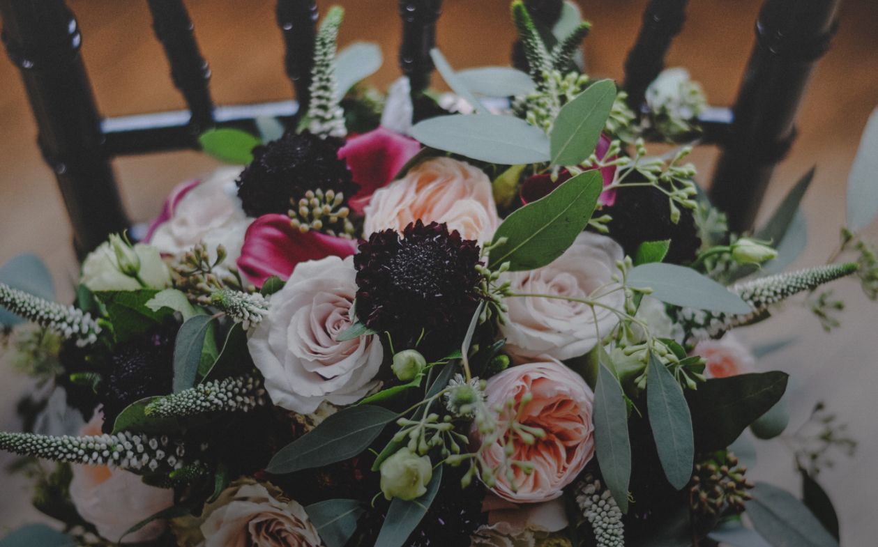 Bouquet of blush and burgundy flowers, greenery, and dark blooms on a black chair.
