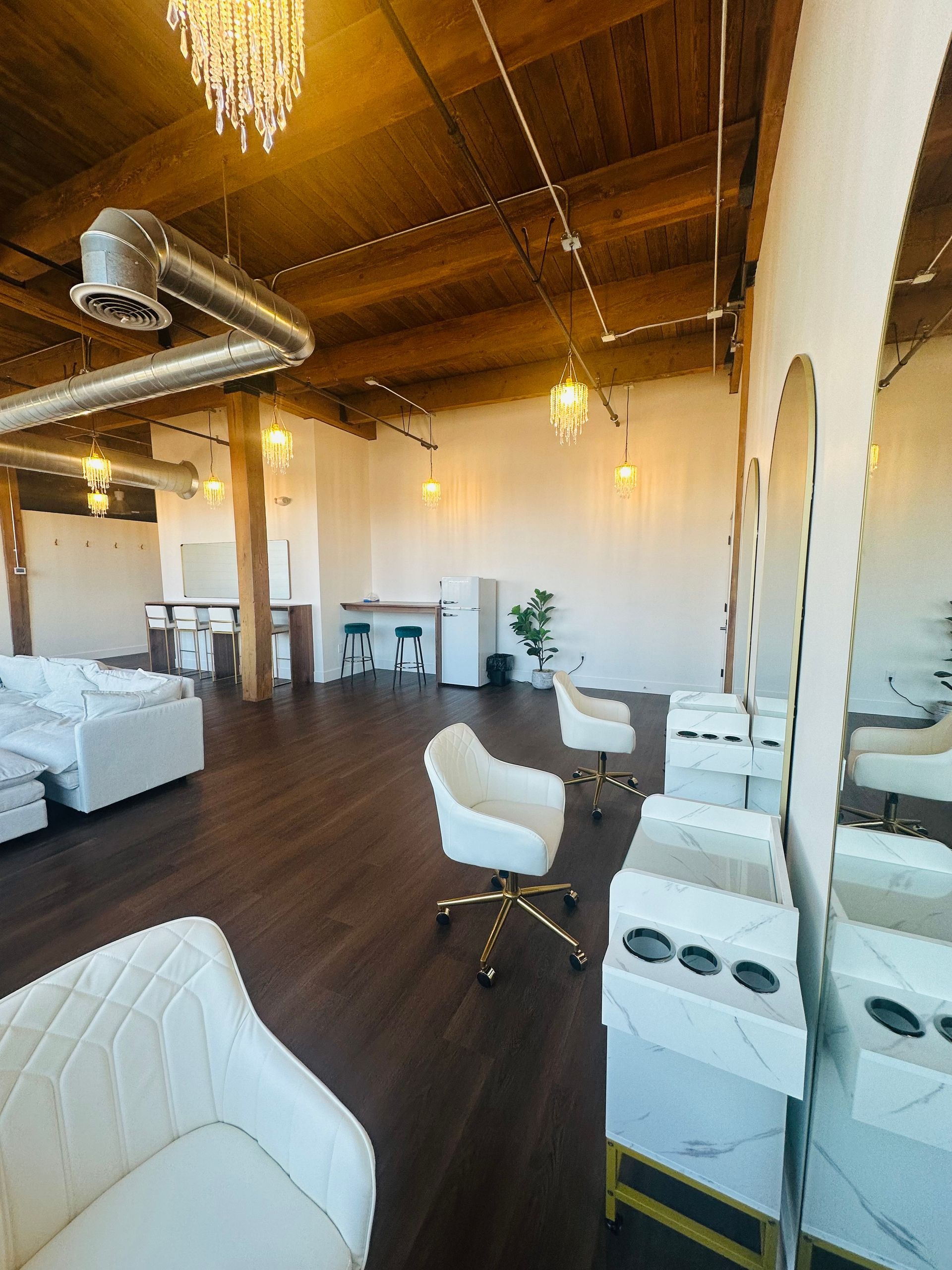 A bright, modern hair salon with white chairs, marble-topped stations, hardwood floors, and exposed ceiling beams.