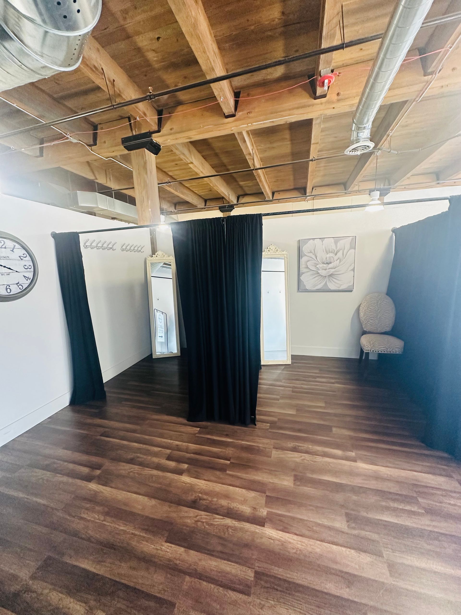 Interior of a loft space with wood ceilings, dark curtains dividing areas, a wall clock, and a light-colored chair.