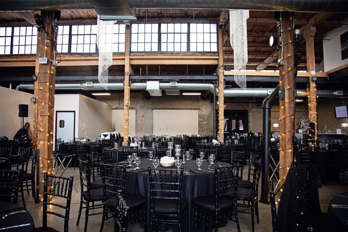 Empty banquet hall with black tables and chairs under exposed wooden beams and tall windows