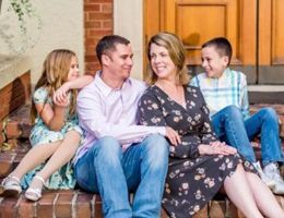 Family of four sitting on brick steps, smiling. Man and woman look at each other, children flanking them.