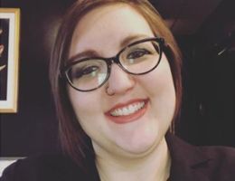 Woman wearing glasses smiles at the camera, wearing a dark blazer.