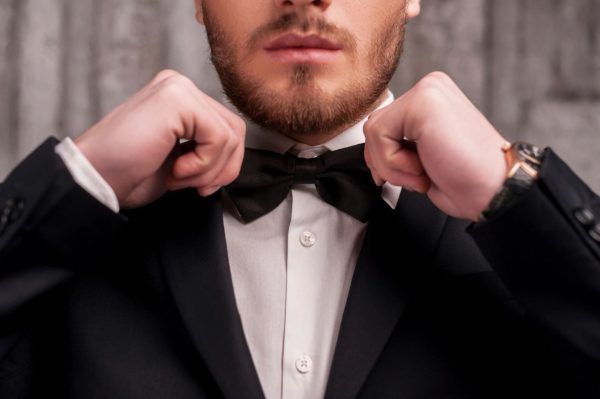 Man adjusting black bow tie, wearing suit jacket and white dress shirt.