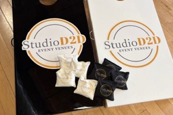 Two cornhole boards with logos, black and white, with bean bags; set on wood floor.