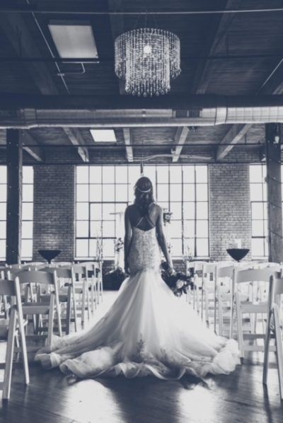 Bride in a wedding dress stands in a large industrial venue with a chandelier.