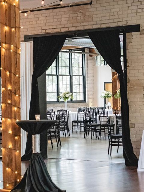 Wedding reception venue with black curtains, brick walls, tables and chairs, and floral centerpieces.