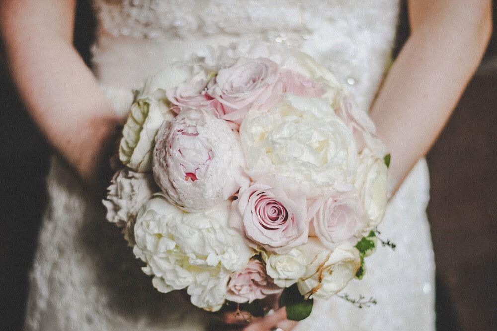 Bride in white lace dress holding a round bouquet of white and pink flowers.