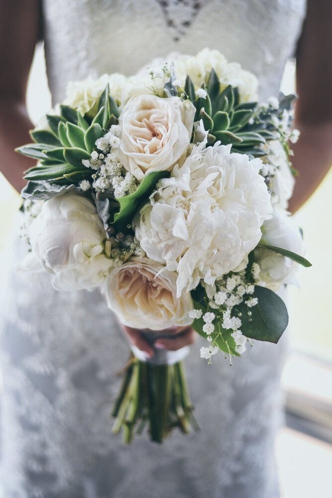Bride holding a white and green floral bouquet with peonies, roses, and succulents.