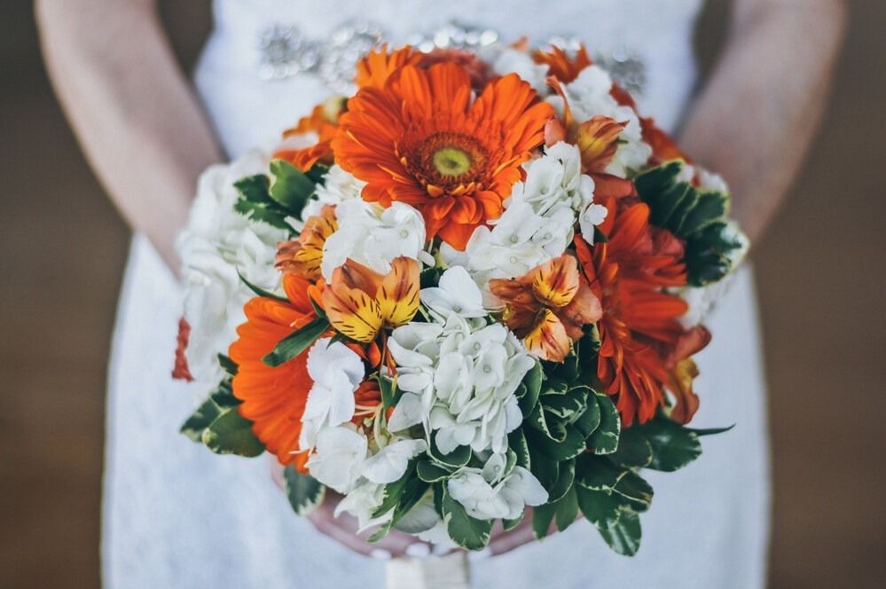 Woman in white dress holding vibrant orange and white floral bouquet.