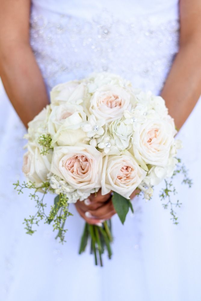 Bride in white dress holding a bouquet of white and peach roses.