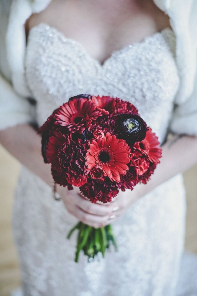 Bride in white lace dress holds a bouquet of red flowers.