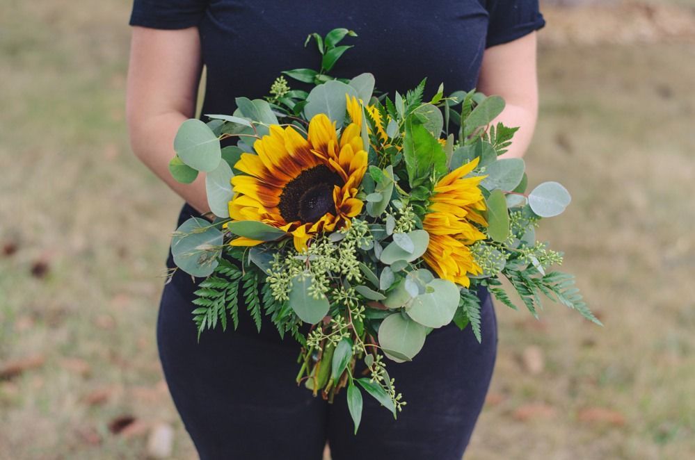 Woman holding a bouquet of sunflowers, eucalyptus, and greenery.
