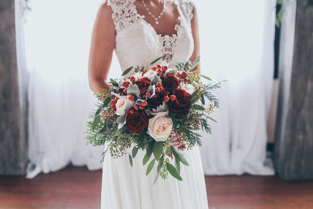 Bride in white lace dress holds a bouquet of red and cream flowers.