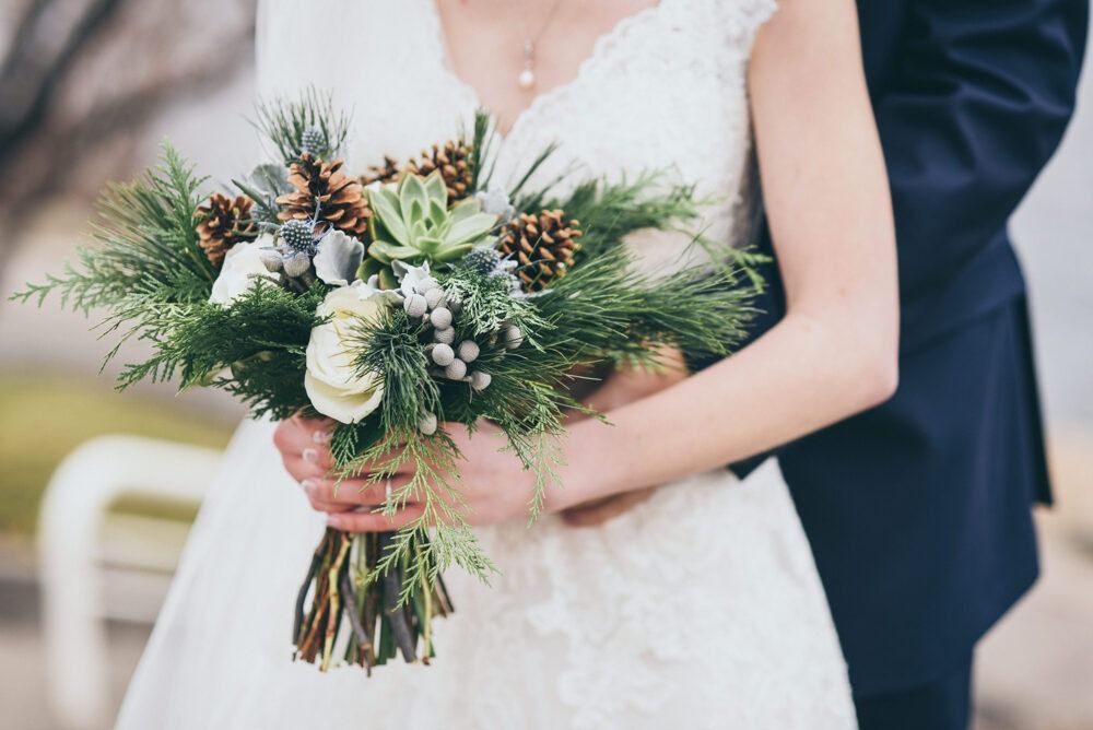 Bride in white dress holds winter bouquet, groom's arms around her.
