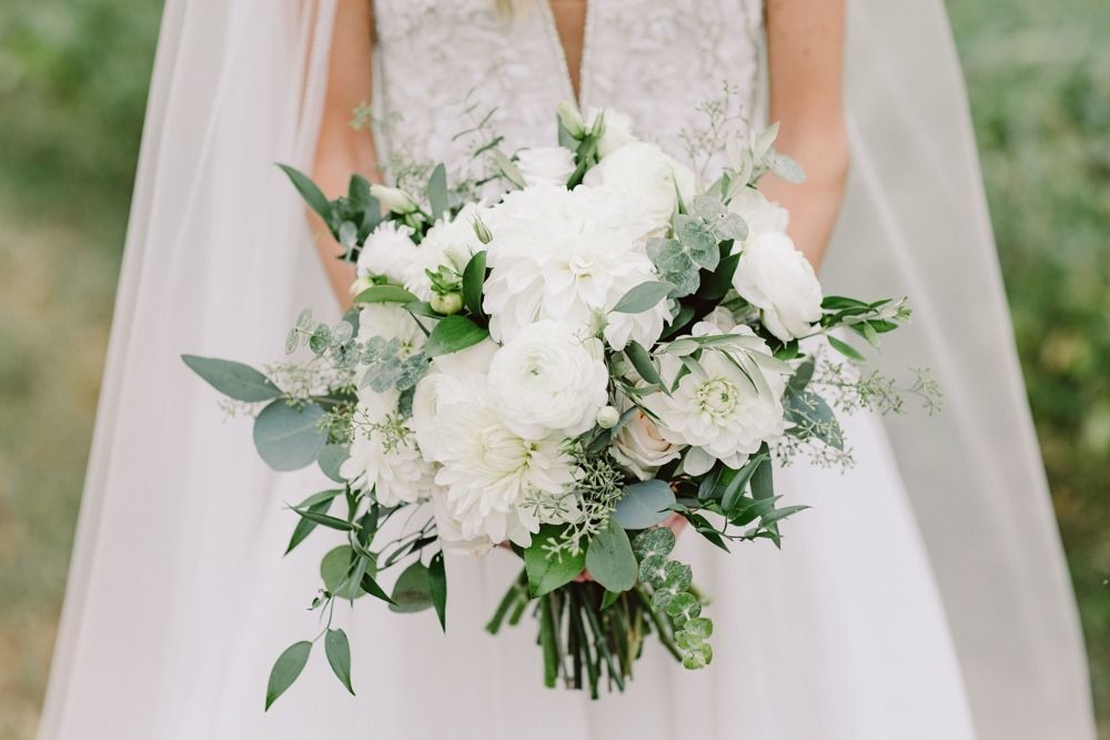 Bride in white dress holding a bouquet of white flowers and greenery.