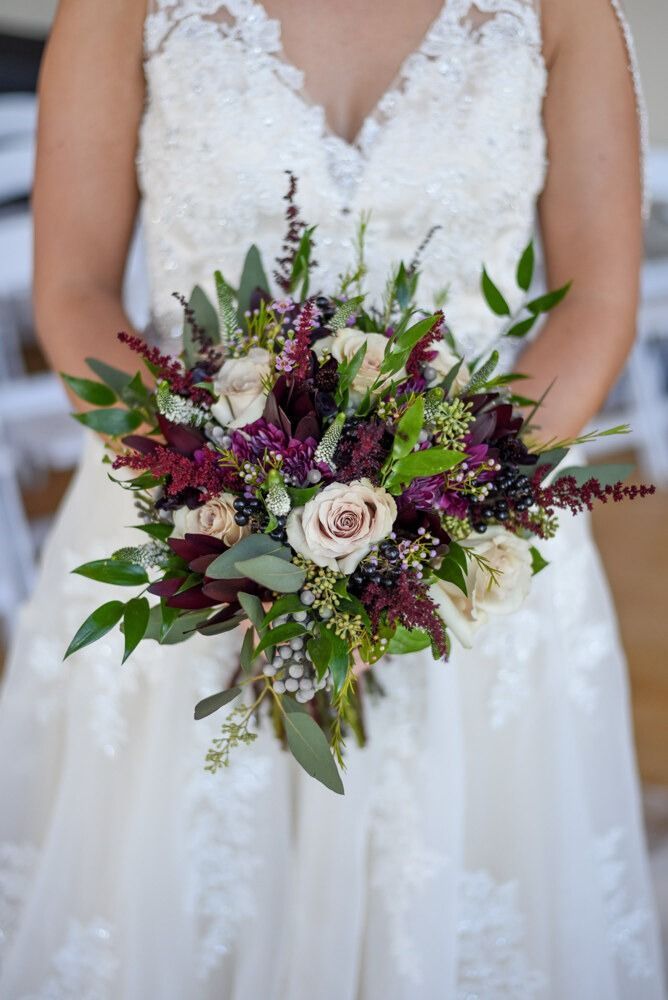 Bride in white lace dress holds a bouquet of white, burgundy, and green flowers.
