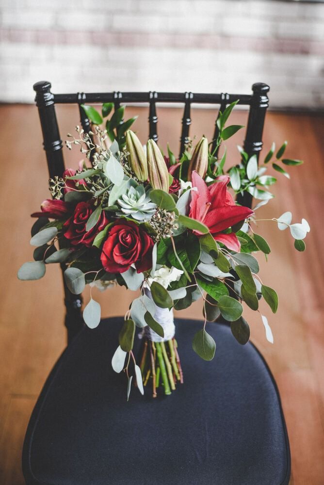 Bouquet of red roses, lilies, and greenery rests on a black chair.