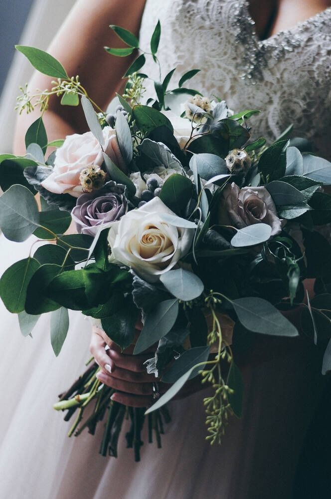 Bride holding a bouquet of roses and greenery, wearing a white wedding dress.
