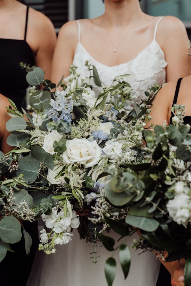 Bride in white dress holding bouquet with blue and white flowers, surrounded by bridesmaids.