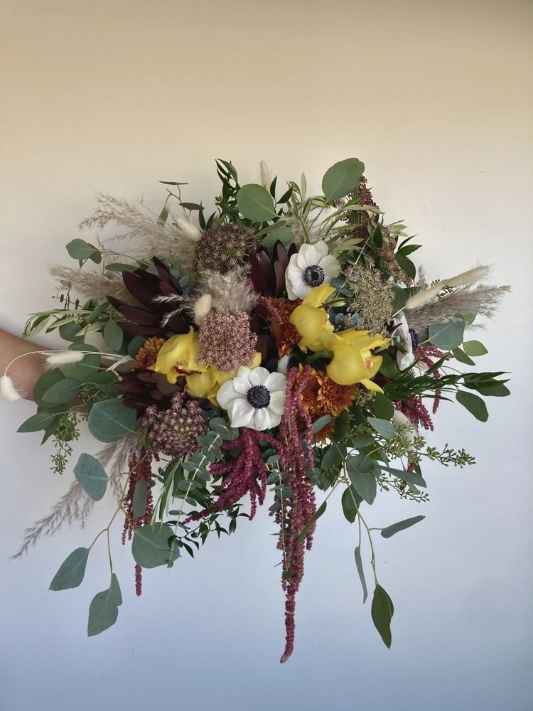 Bouquet of white anemones, yellow flowers, burgundy and rust hues, and green foliage.