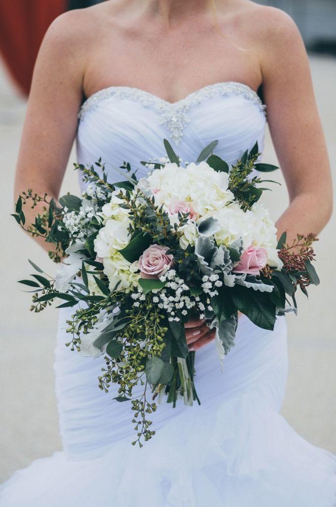 Bride holding bouquet of white and pink flowers, wearing a strapless, white wedding dress.