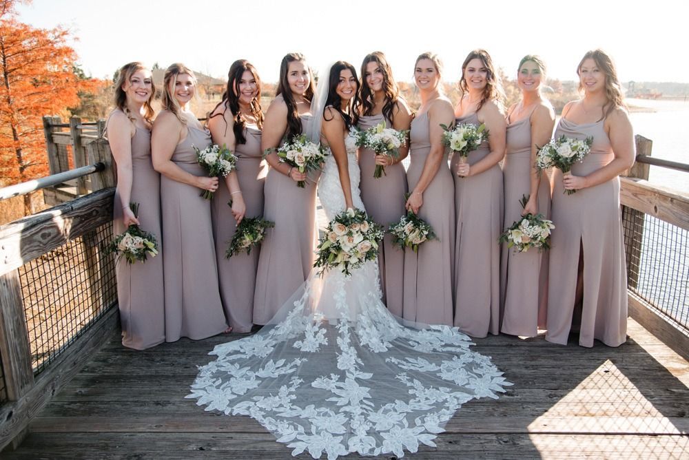 Bride with bridesmaids on a wooden dock; all wearing dusty rose gowns, holding bouquets.