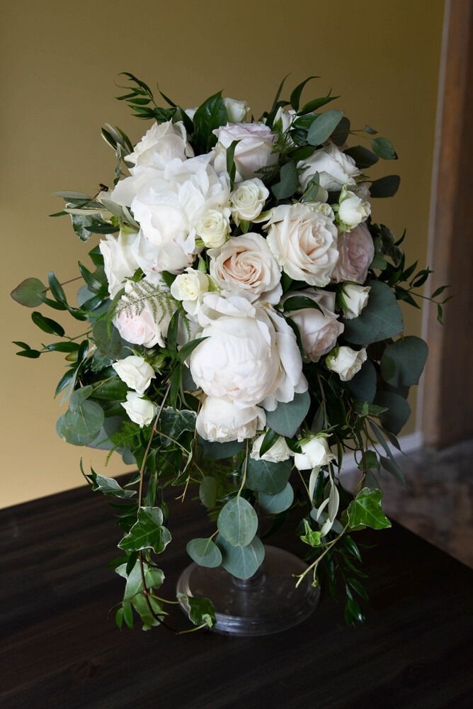 Elegant white and blush floral arrangement with greenery, displayed in a clear vase on a table.