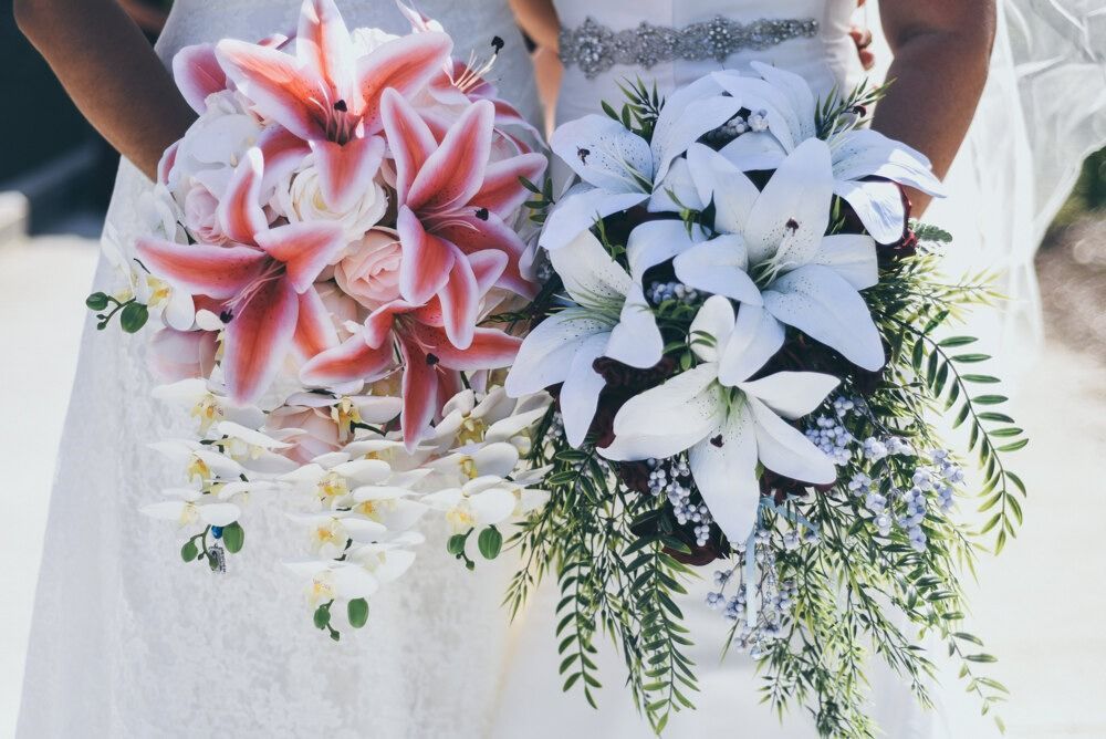Two brides holding bouquets of white and pink lilies and orchids.