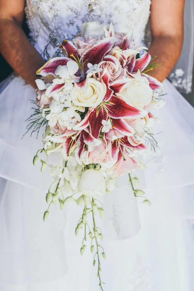 Bride holding cascading bouquet of white roses and maroon lilies.