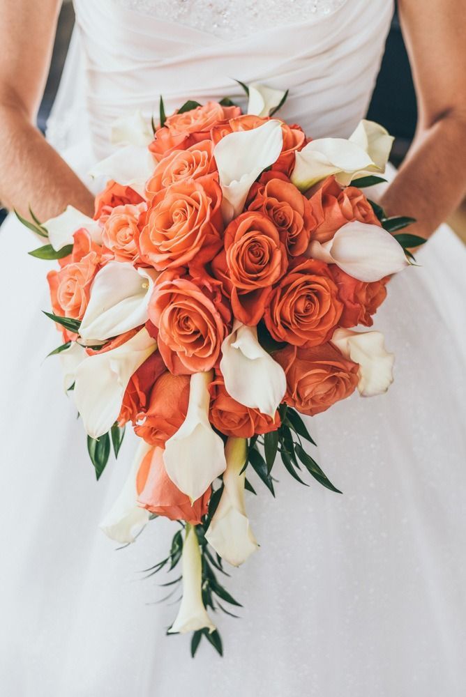 Bride holding a cascading bouquet of orange roses and white calla lilies.
