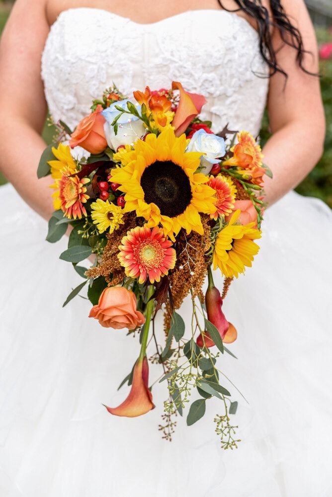 Bride holding a vibrant fall bouquet with sunflowers, orange roses, and calla lilies.