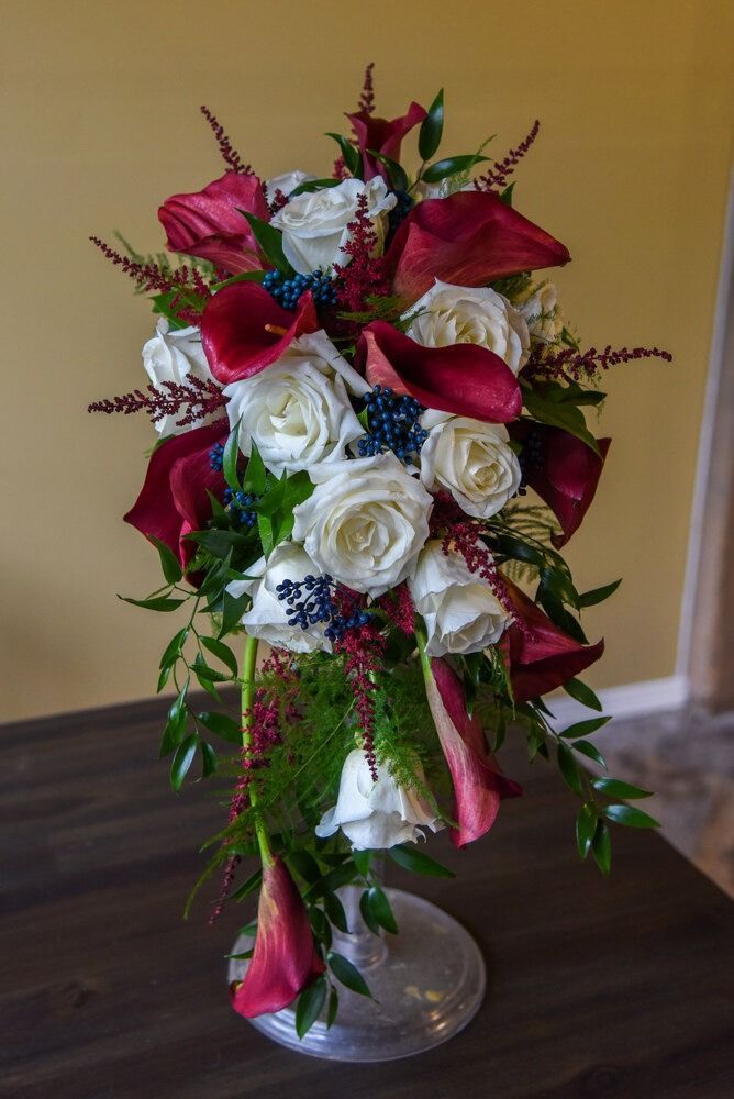 Cascading bouquet of white roses and dark red calla lilies in a vase on a wooden surface.