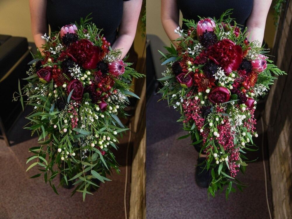Woman holding a cascading bouquet of red flowers, greenery, and white accents.