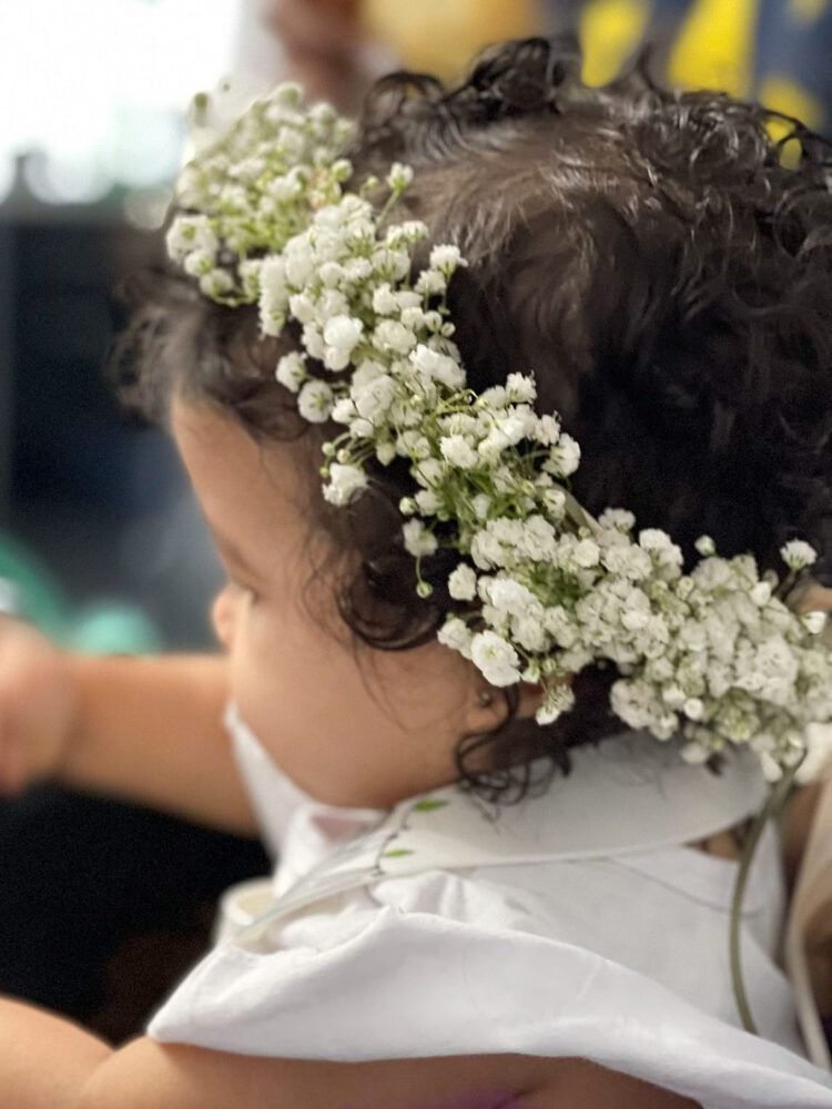 Child with dark, curly hair wearing a white flower crown and white collared shirt.