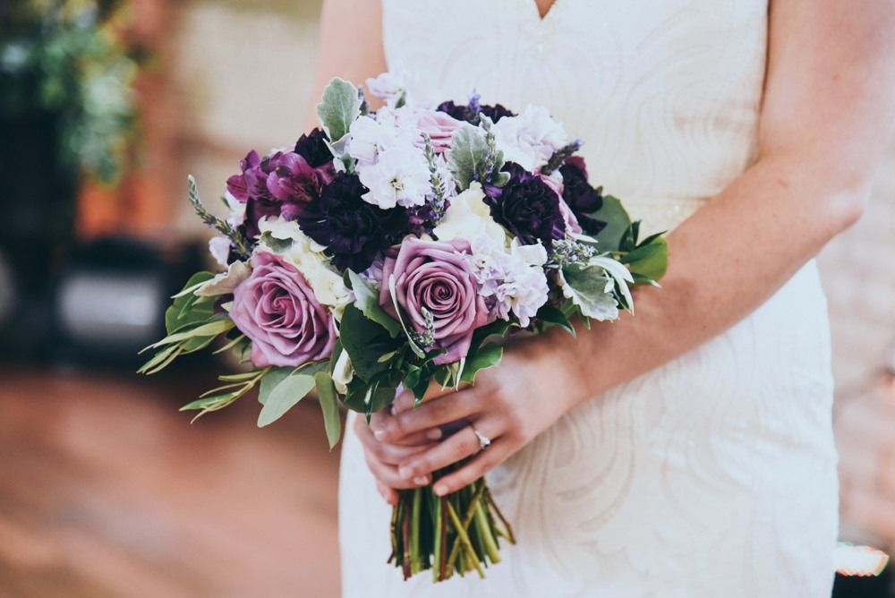 Woman in white dress holding a bouquet with purple and white flowers.