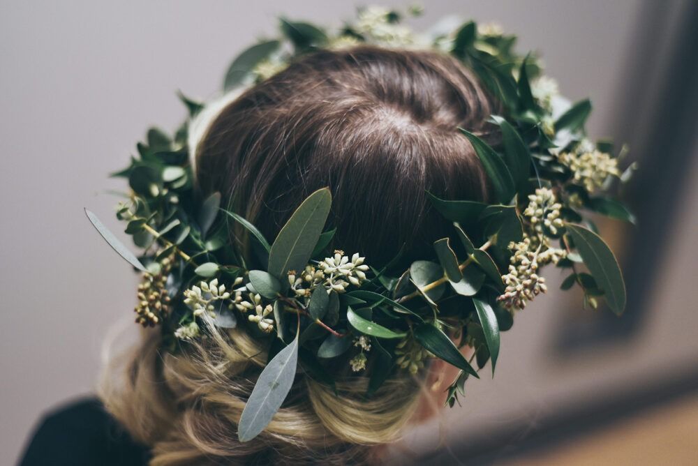 Woman's head with a green floral crown. Blonde hair is styled in an updo.