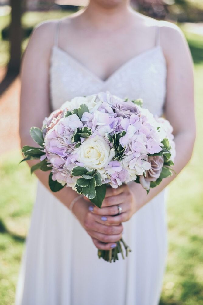 Bride in white dress holding a bouquet of light purple and white flowers.