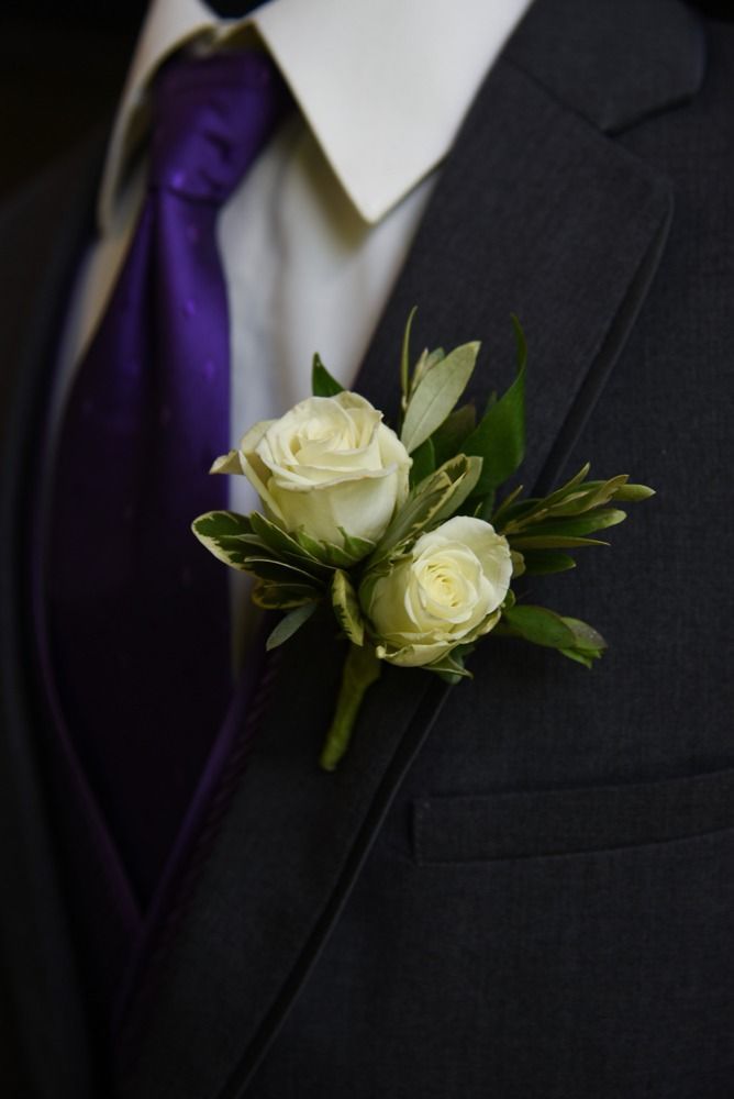 White rose boutonniere on a dark suit with a purple tie.
