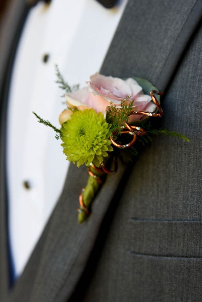 Boutonniere of pink rose and green flower on a gray suit jacket.