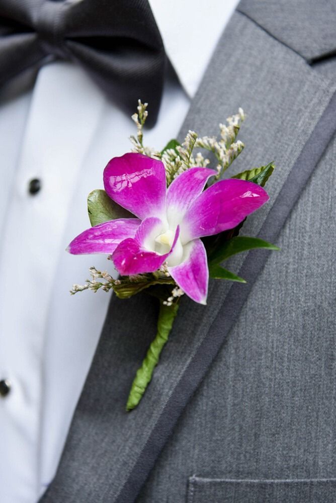 A vibrant purple orchid boutonniere on a gray suit jacket, next to a white shirt and black bow tie.