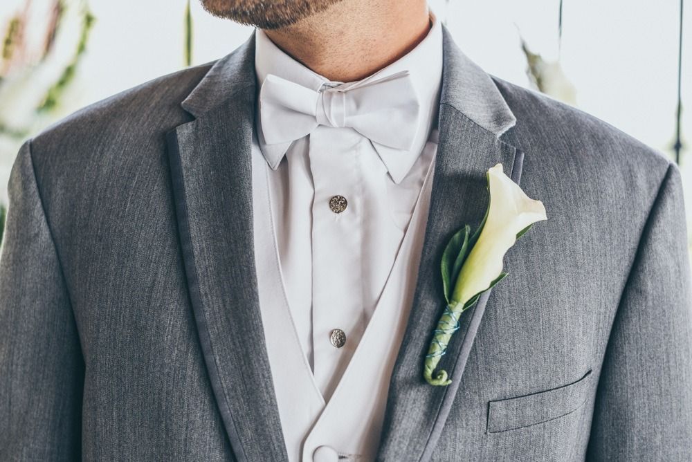 Man in a gray suit with a white bow tie, vest, and flower boutonniere.