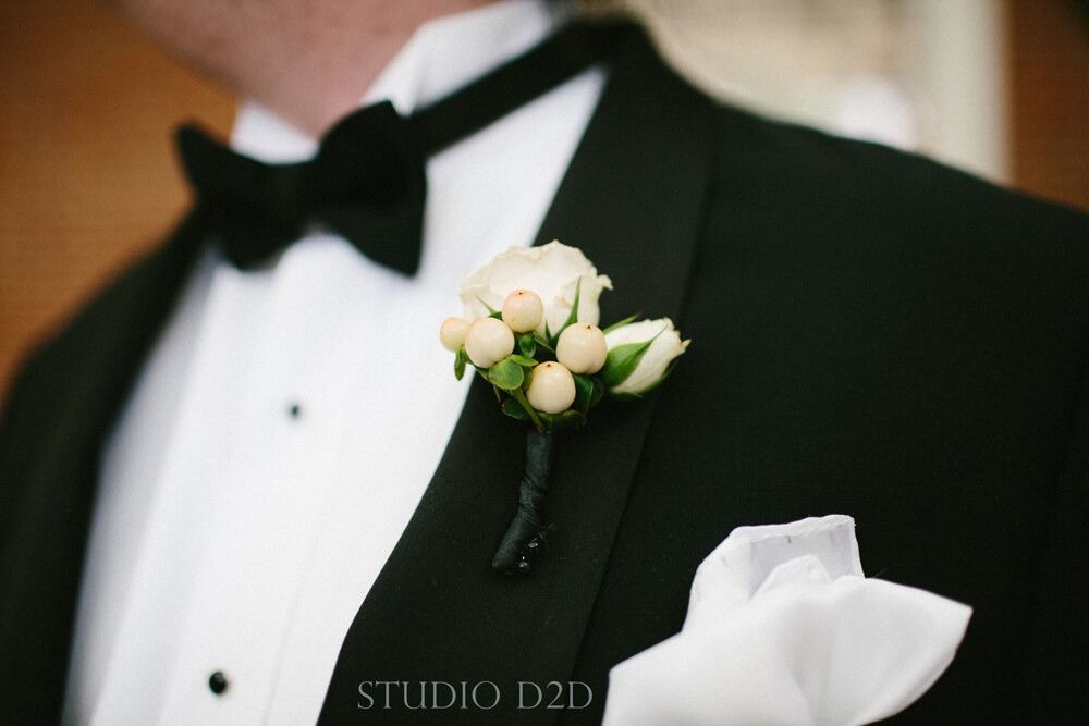 Close-up of a man in a tuxedo with a white rose boutonniere and pocket square.