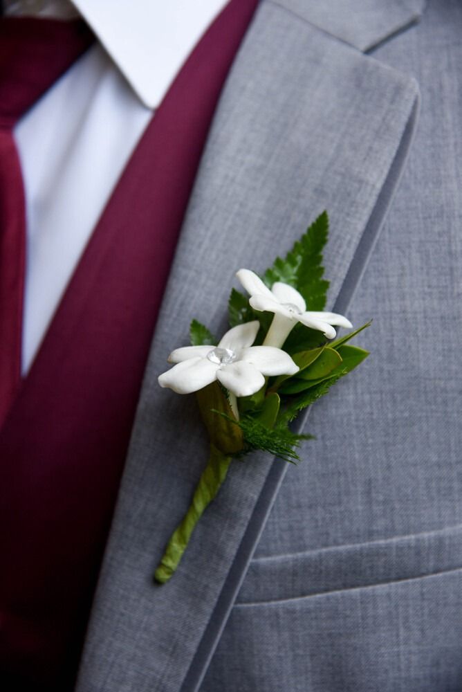 White boutonniere on gray suit, burgundy vest and tie visible.