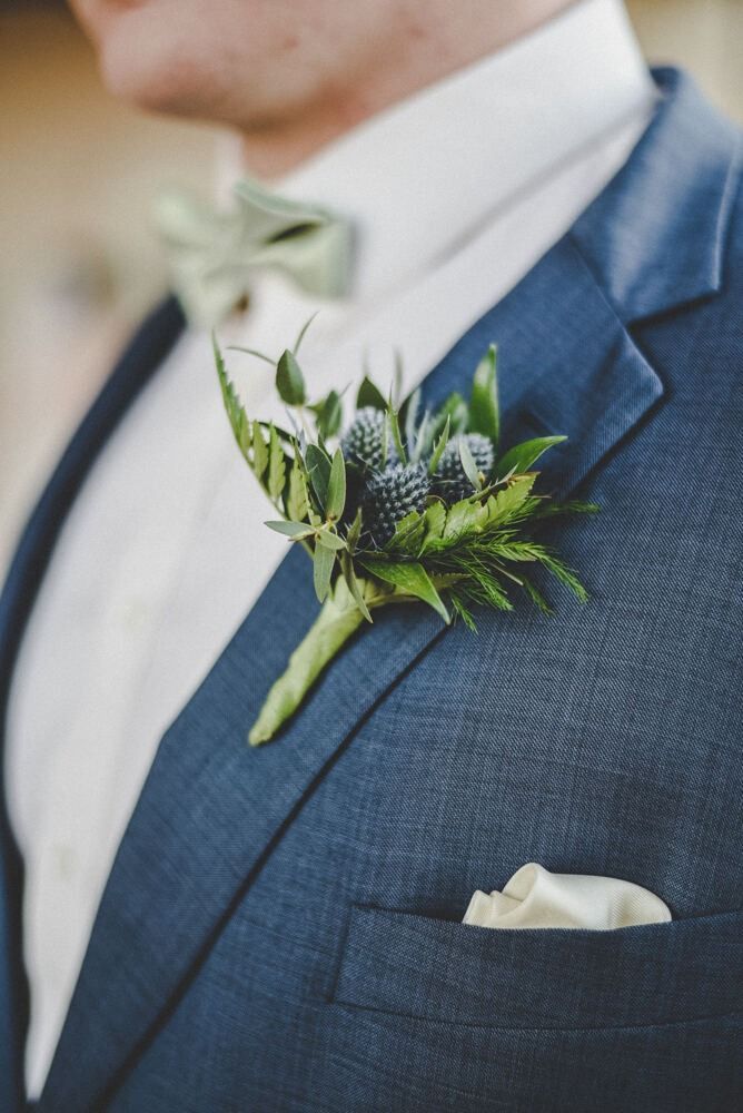 Man in blue suit with green bow tie and boutonniere. Pocket square visible.