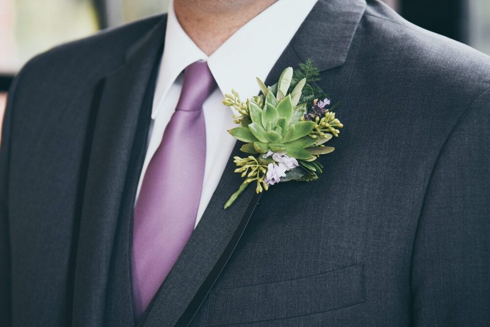 Man in gray suit with purple tie and succulent boutonniere.