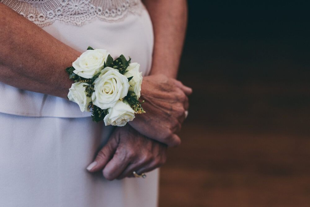 Woman's hands with white floral wrist corsage, wearing a white dress.