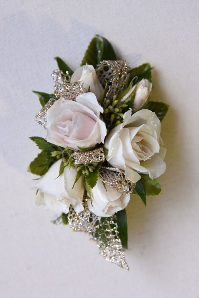 White rose corsage with silver glitter accents and green leaves.