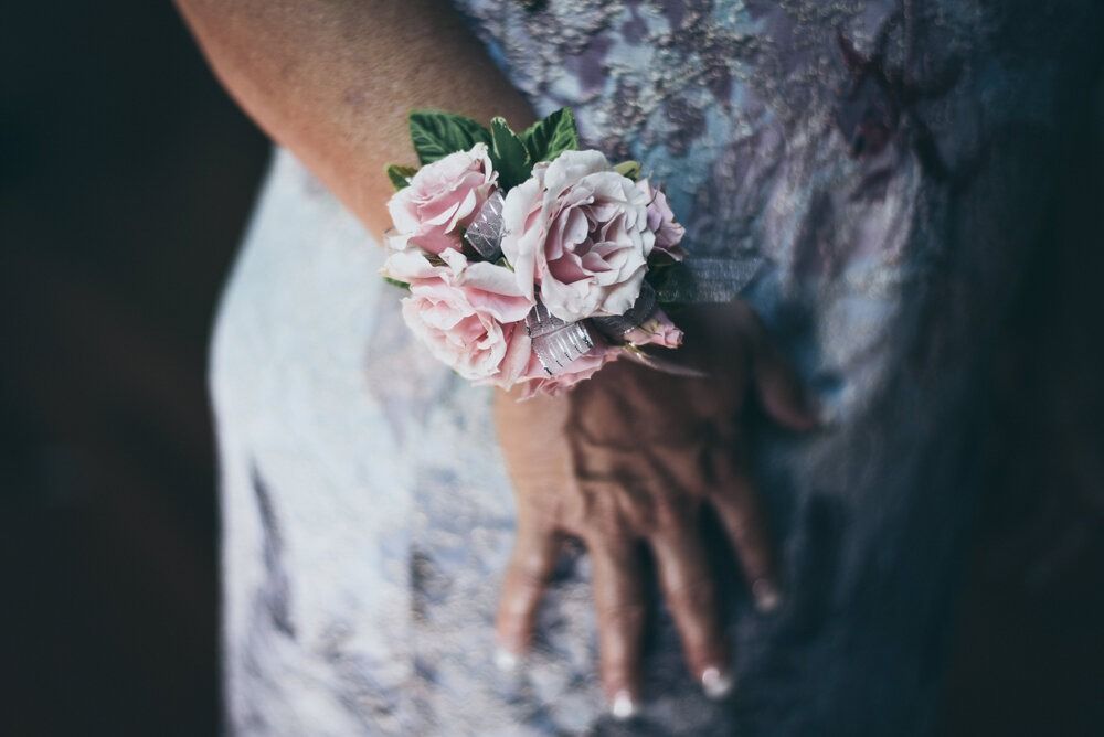 Wrist corsage of pink roses on a person's wrist, near a light-colored patterned dress.