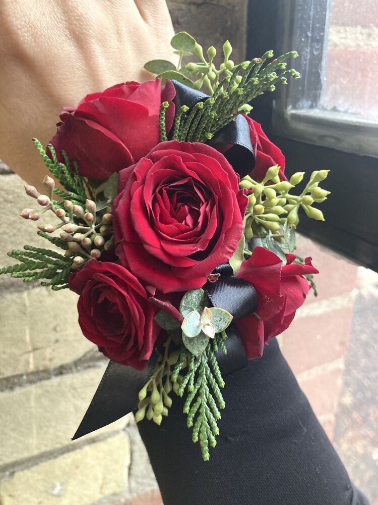 Wrist corsage of red roses with greenery and black ribbon.